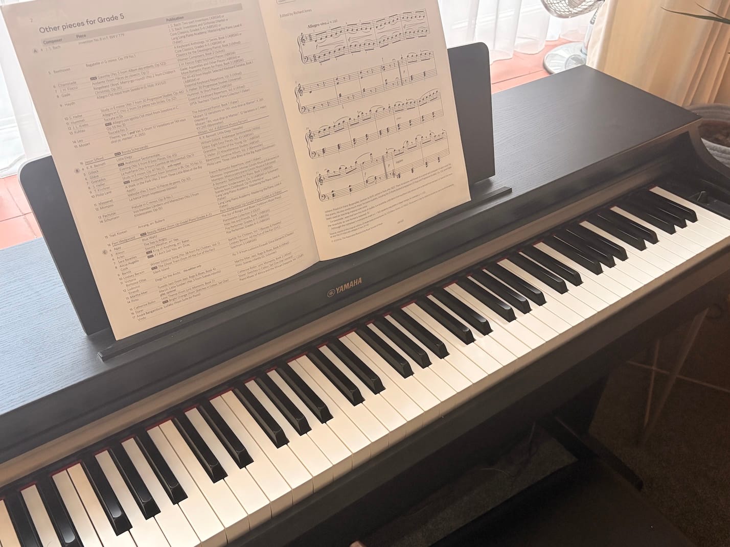 A photo showing a black digital piano with a piece of grade 5 sheet music on the stand.